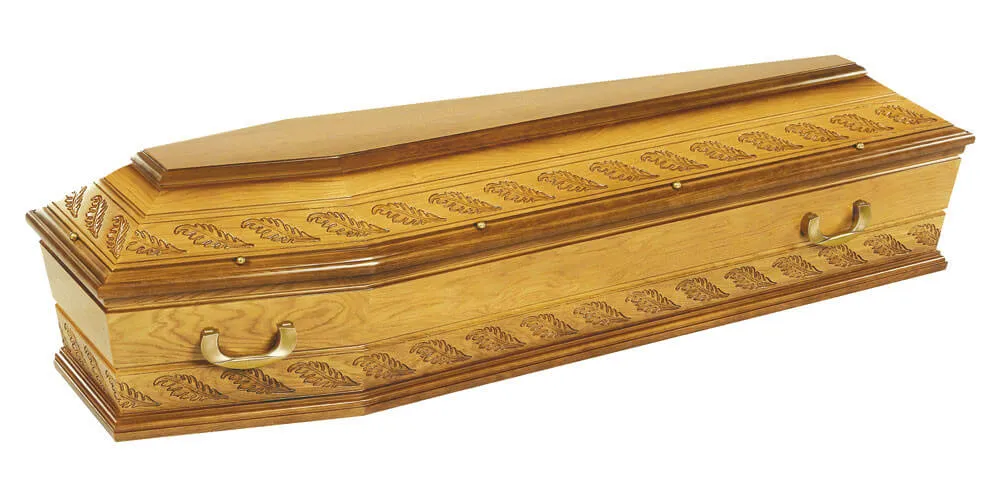Cercueil en bois clair gravé de motifs de feuilles sur la bordure supérieure et inférieure.